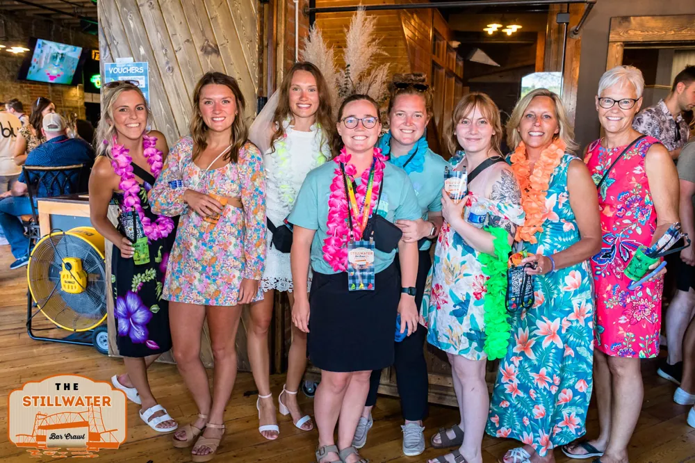Eight friends in leis and floral dresses celebrating at The Stillwater Bar Crawl