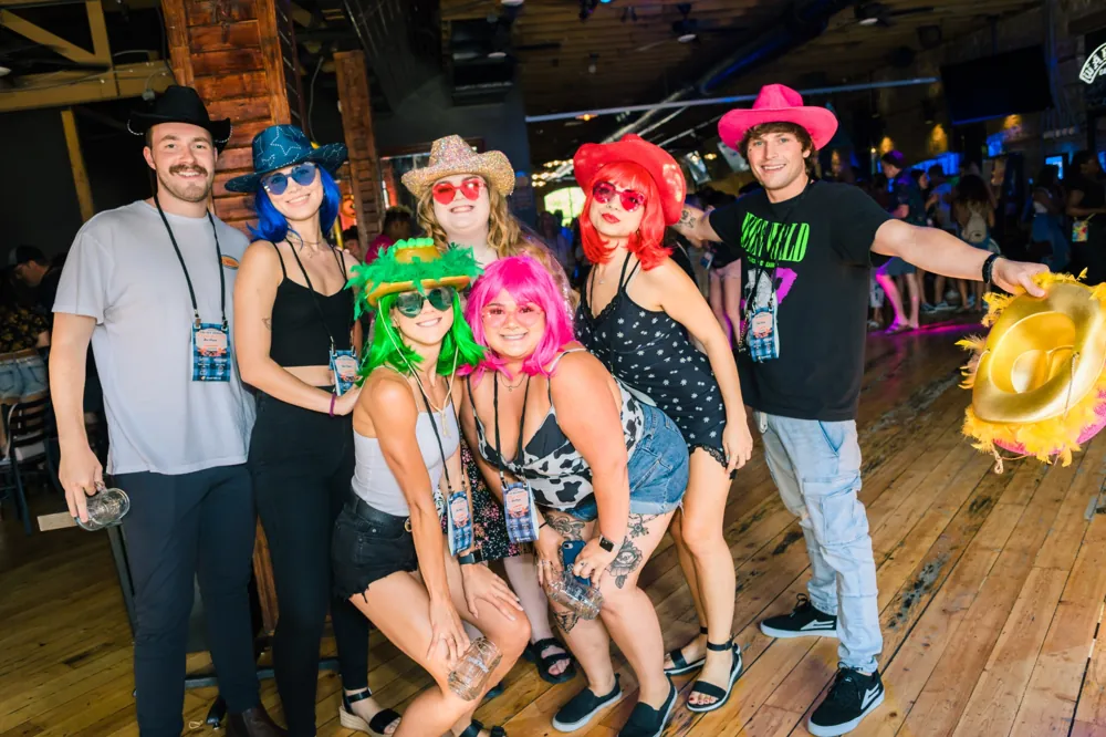 Friends in colorful wigs and cowboy hats on the dance floor at The Stillwater Bar Crawl