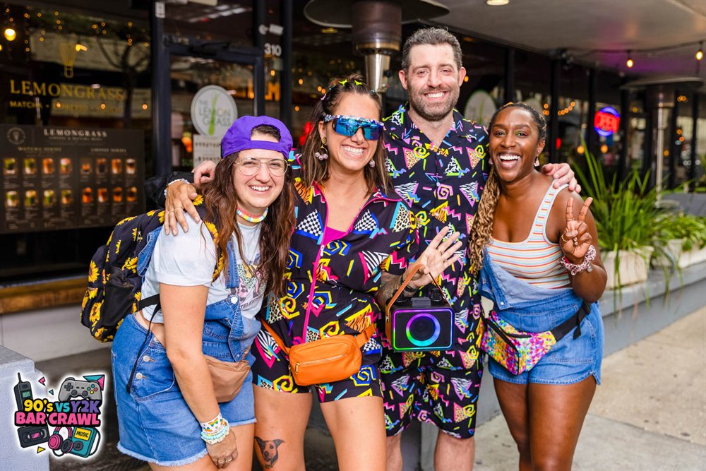 Four friends in retro 90s prints carrying a karaoke speaker at the 90s vs Y2K Bar Crawl