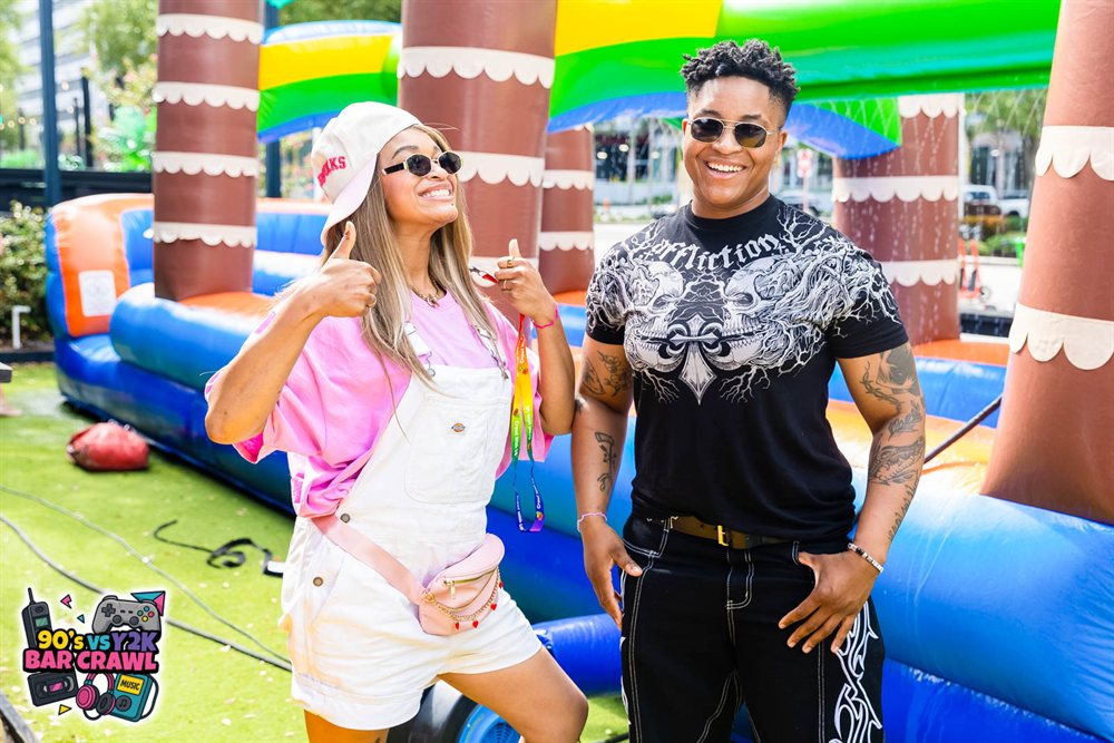 Two crawlers giving thumbs-up in front of the inflatable water slide at the 90s vs Y2K Bar Crawl