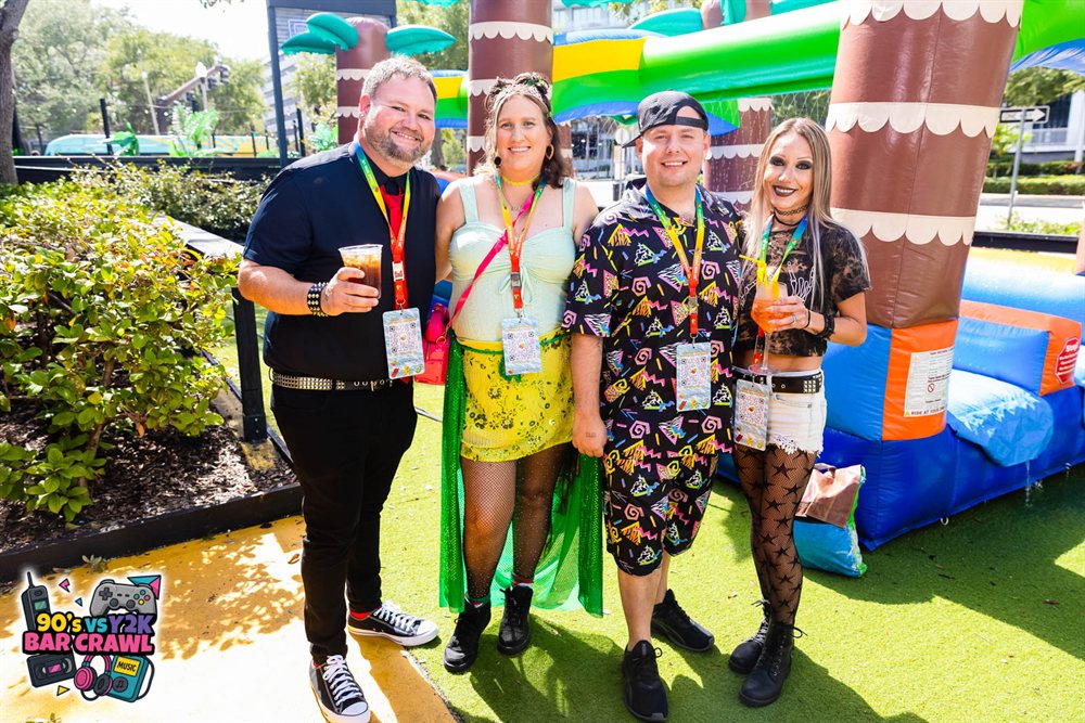 Four friends with official badges and lanyards at the 90s vs Y2K Bar Crawl inflatable