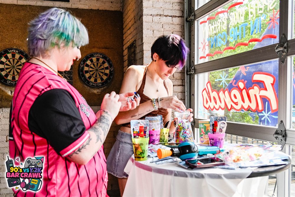 Two crawlers making friendship bracelets at the 90s vs Y2K Bar Crawl merch table