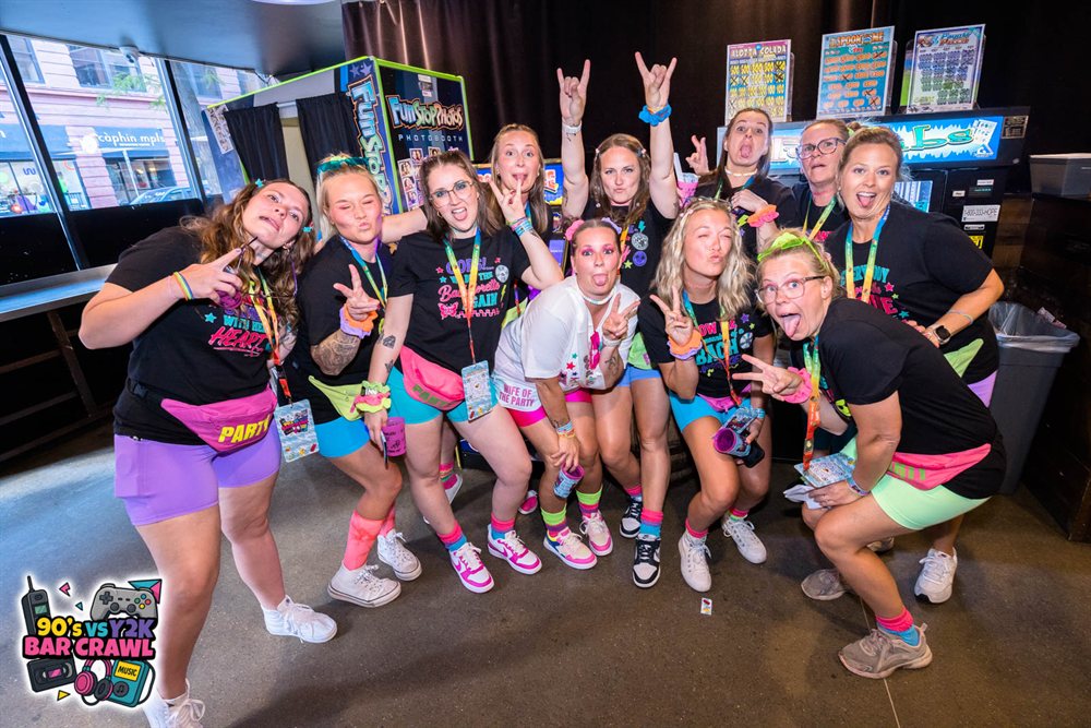 Bachelorette party in matching shirts and neon fanny packs at the 90s vs Y2K Bar Crawl photo booth