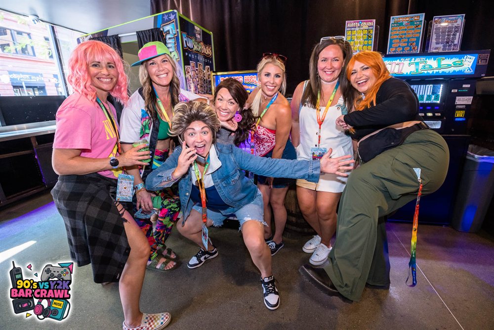 Friends in wigs and 90s costumes striking a pose at the 90s vs Y2K Bar Crawl photo booth